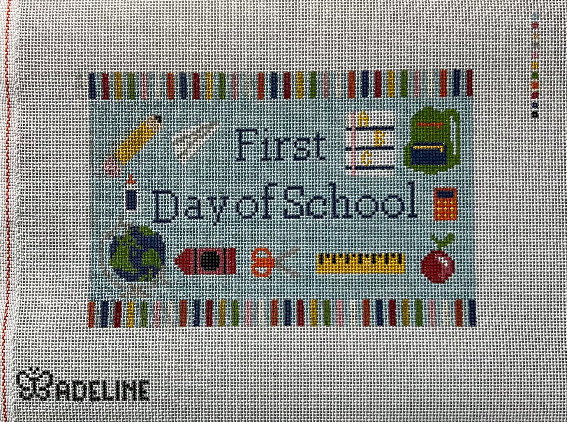 A needlepoint canvas on 13 mesh canvas, featuring the text 'First Day of School' surrounded by school-themed icons like a pencil, globe, books, and ruler.